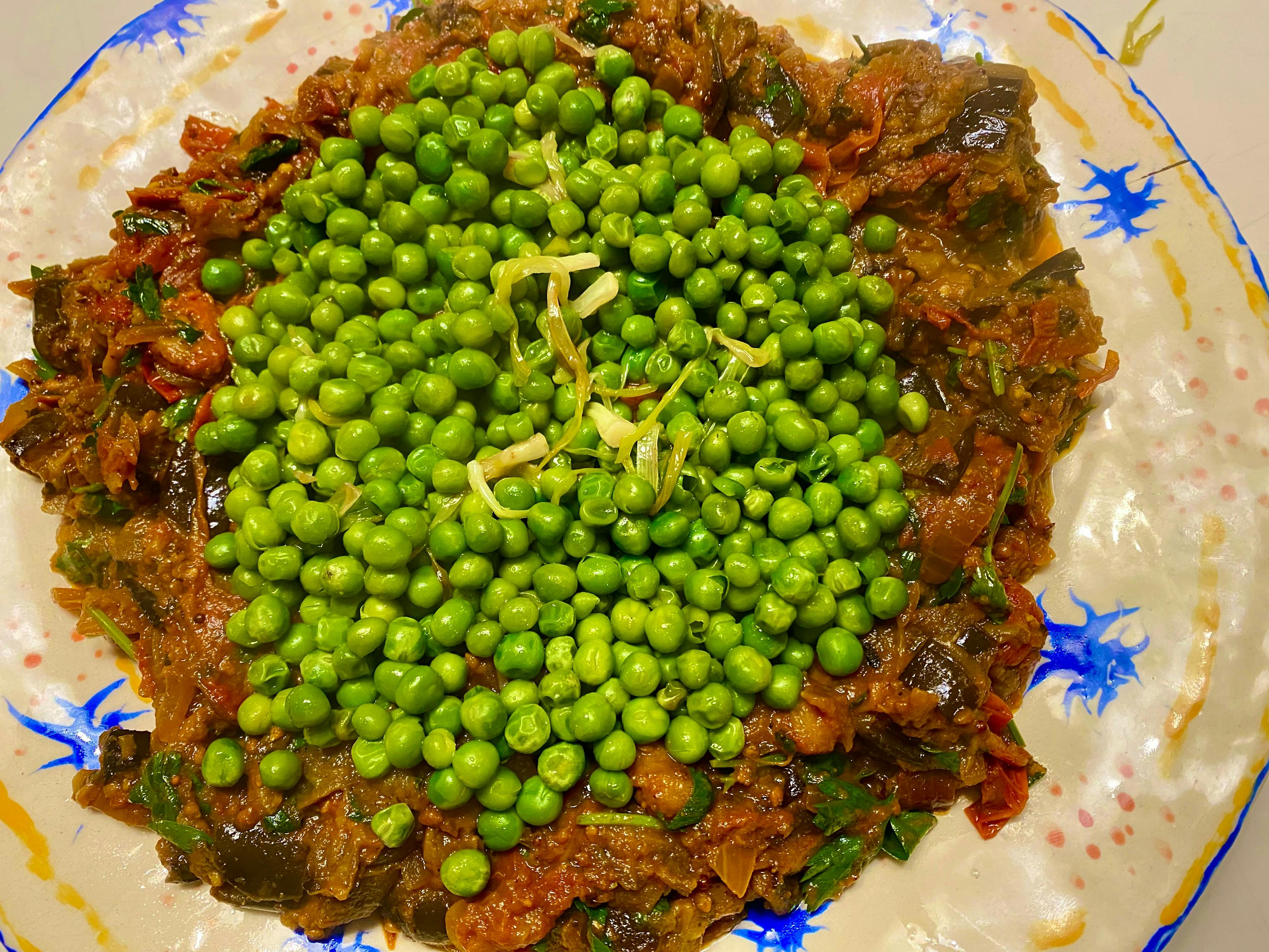 plate with aubergine and tomato mixture with fresh peas on top