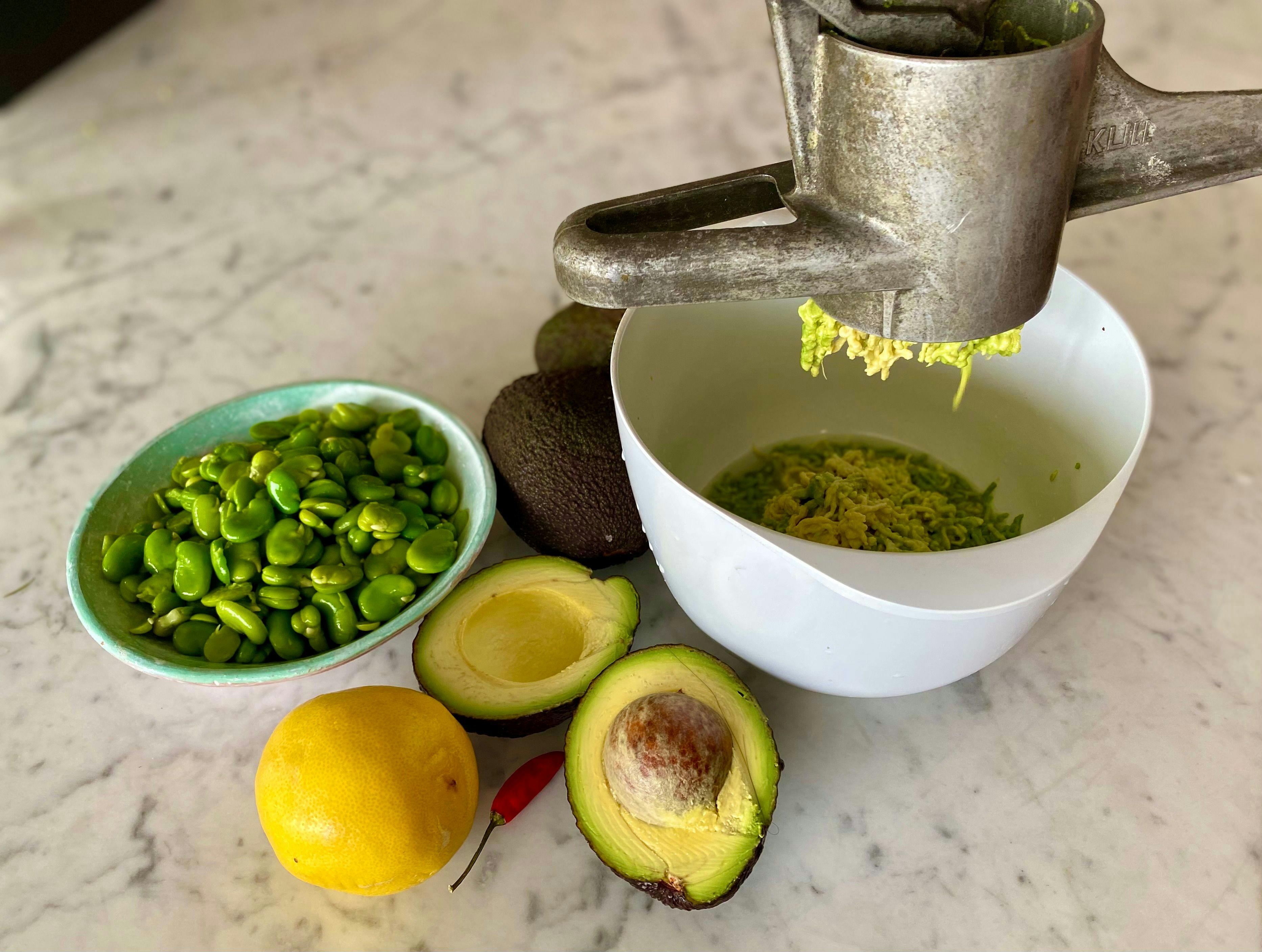 bowl of peeled broad beans avocados lemon and potato ricer and bowl