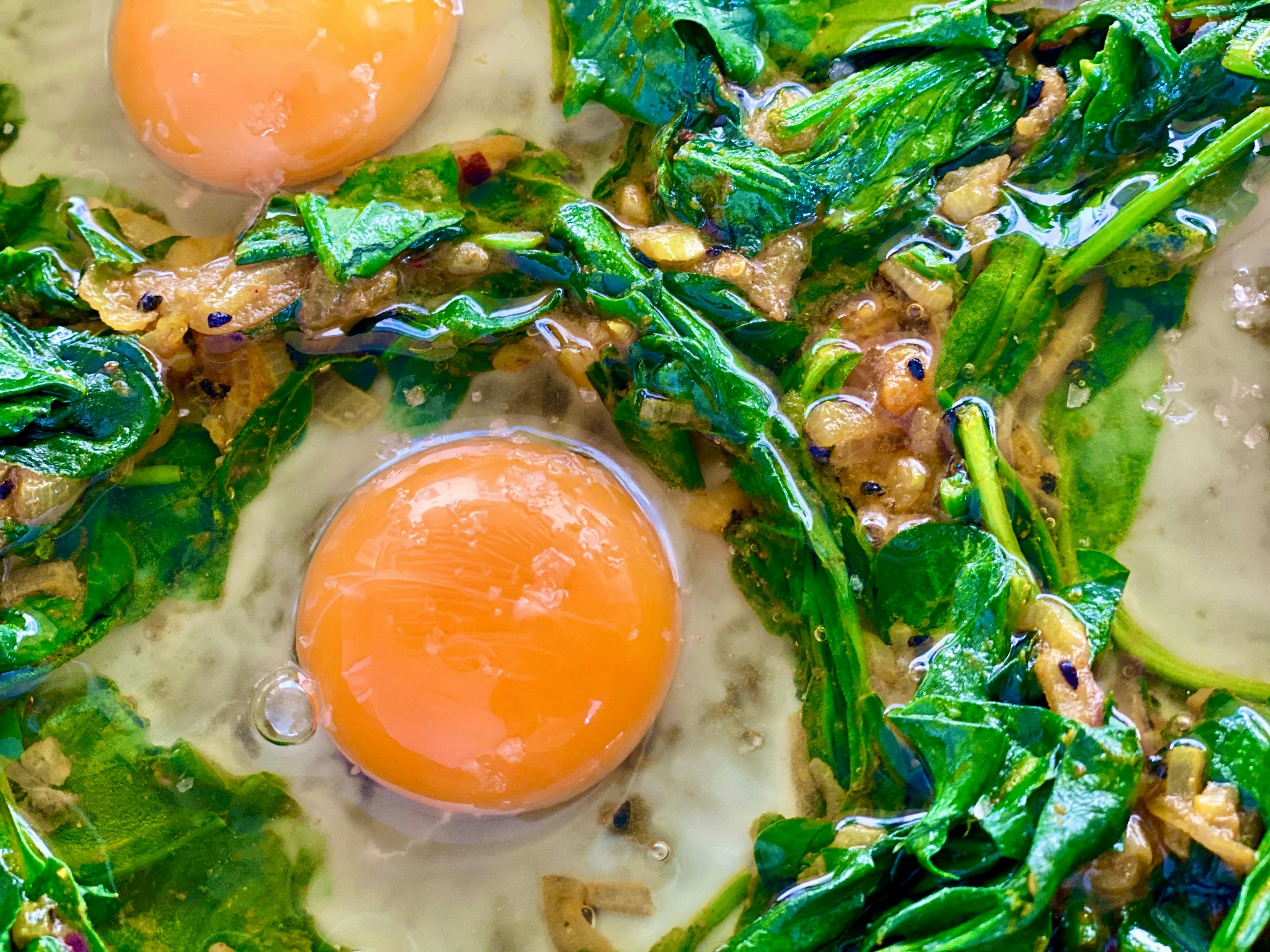 eggs placed in little wells of spinach in saucepan