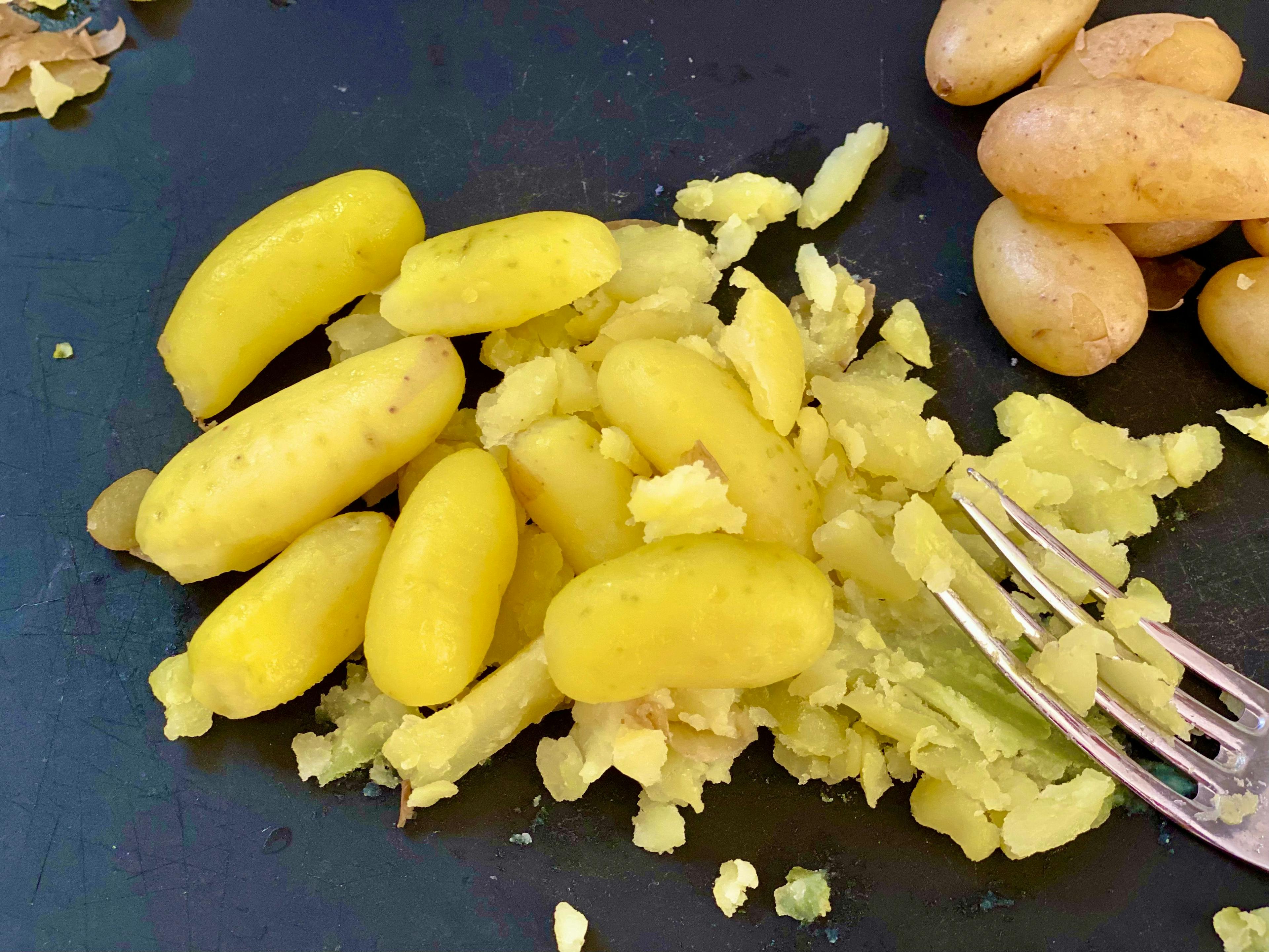 little peeled potatoes being smashed with a fork